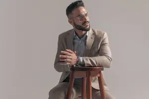 A man in a suit and glasses sitting on a stool