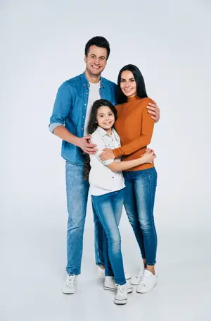 A man, a woman, and a young girl stand close together, smiling and posing for a photo.