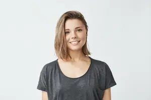 A smiling woman with short blonde hair wearing a black T-shirt against a white background