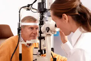 Senior man looking into an ophthalmoscope while a doctor looks on