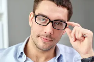 A man wearing a watch and glasses is adjusting his glasses.