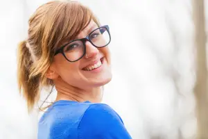 A smiling woman wearing glasses and a ponytail, looking at something in front of her