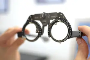 A person adjusting a pair of black frame spectacles with a number dial on the side.