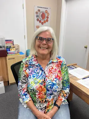 Woman sitting in office chair with colorful shirt and smiling