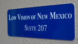 A blue sign on a wall reads 'Low Vision of New Mexico Suite 207'.
