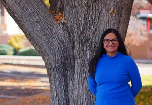 woman wearing a blue shirt leaning against a tree in an outdoor area