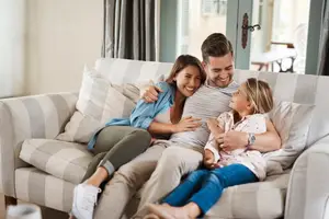 A happy family of three sitting on a couch together in a cozy living room.
