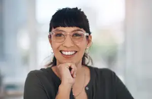 Portrait of a smiling woman wearing glasses, seated indoors.