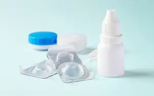 A white eye drop bottle, two contact lens cases, and a blue lid are displayed on a blue background.
