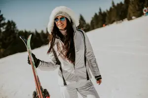 A smiling woman in a white winter jacket poses with skis in a snowy landscape.