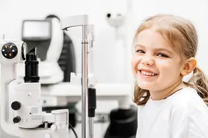 A smiling young girl is having her eyes examined by an optometrist in a clinic.