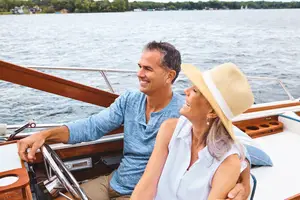 A man and woman are on a boat smiling at each other with the ocean behind them