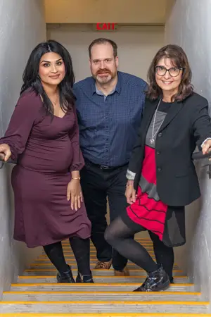 Three people are standing on a staircase, smiling and posing for a photo.