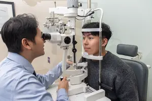 An optometrist checks a patient's eye using an ophthalmoscope in a medical office.