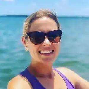 A woman smiling and posing for a photo on the beach with the ocean in the background.