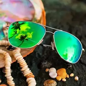 Sunglasses with green lenses reflecting palm trees are placed on a rustic wooden surface near seashells and a pearl shell.