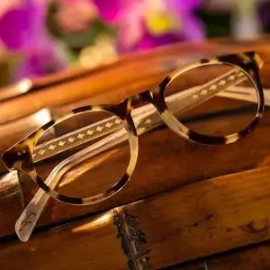 A pair of brown-framed eyeglasses with star patterns on the sides is displayed on a wooden surface, possibly in a room with dim lighting and a blurred background.