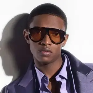 A man in a purple coat and sunglasses is posing for a photo.