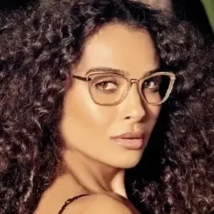 Close-up of a woman with curly hair and glasses posing for a photo