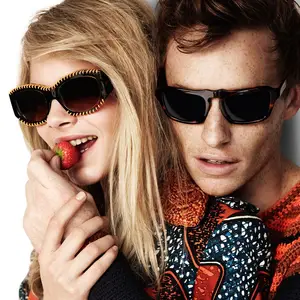 A man and a woman wearing sunglasses, the woman holding a strawberry and smiling while the man looks at her