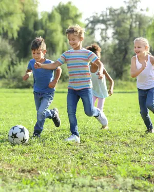 Four children playing soccer on a grassy field with trees in the background