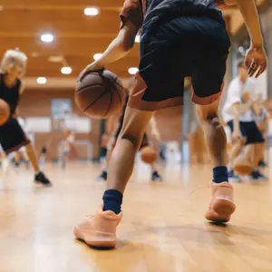 Two kids playing basketball in a gym, one of them dribbling the ball.