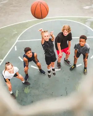 Five children play basketball on a court, with one boy leaping to catch the ball