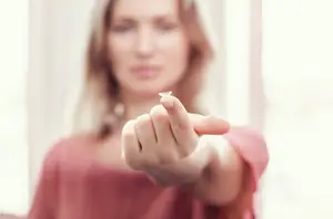 A woman wearing a pink shirt and pointing to a contact lens she is holding in her hand
