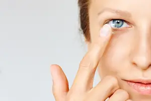 A woman wearing a contact lens in her eye and placing a finger on her eye.