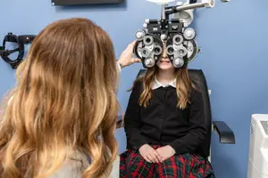 A young girl is getting her eyes examined by a woman in a blue room