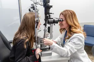 An optometrist checks a young patient's eyes using an ophthalmoscope