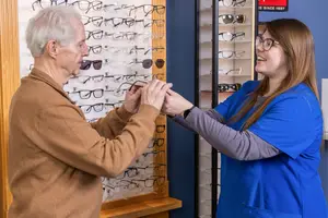 A senior man trying on a pair of glasses while a woman with glasses smiles at him in an optical shop