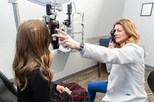 A woman in a white coat examining a young girl's eyes with an ophthalmoscope