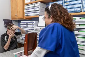 A woman in a blue lab coat is examining a boy's eyes in a medical office.