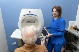 A medical professional is helping an elderly patient use a medical imaging machine in a clinic setting.