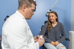 A doctor examines a model eye with a young woman in a medical office