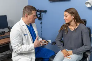 A doctor explains something to a patient about an eye model in a medical office.