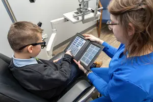 A boy is having an eye exam with a woman who is assisting him.