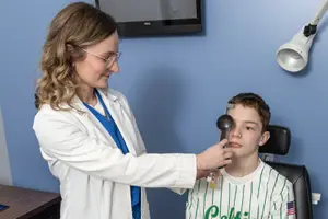 A doctor in a white coat is examining a young boy's eyes in a medical clinic setting.