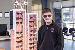 A smiling man stands behind a Maui Jim sunglasses display in a store.