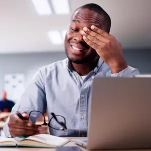 man sitting at laptop rubbing dry eyes