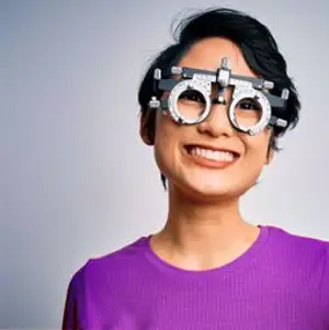 A smiling woman with black hair and eyeglasses wearing purple shirt and smiling at the camera