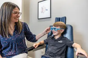 A woman adjusts a boy's glasses in a medical setting.