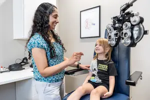 A woman is doing a vision test with a young girl sitting in front of her in a medical clinic.