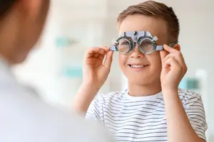 A boy in a striped shirt is holding a pair of trial frame glasses while looking at someone.