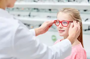 A young girl is having her eyeglasses adjusted by a woman in a white coat in a store