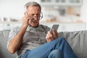 old man sitting on couch struggling to read text on phone 