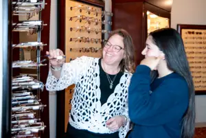 Two women are smiling and looking at a display of eyeglasses in a store.