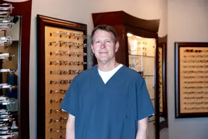 A man in a blue shirt stands in front of a wall with several frames displayed on it.