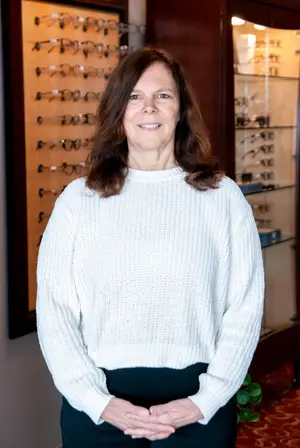 A woman with brown hair wearing a white sweater standing in front of a display case of glasses.